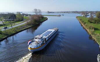 A boat named Lena Maria cruises on a calm canal surrounded by greenery and a road.