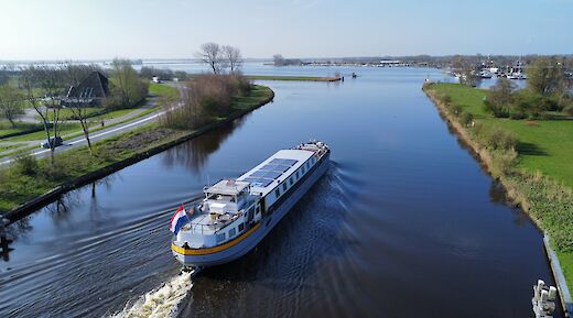 A boat named Lena Maria cruises on a calm canal surrounded by greenery and a road.
