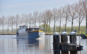 A boat named Lena Maria approaches on a canal with a line of trees in the distance.