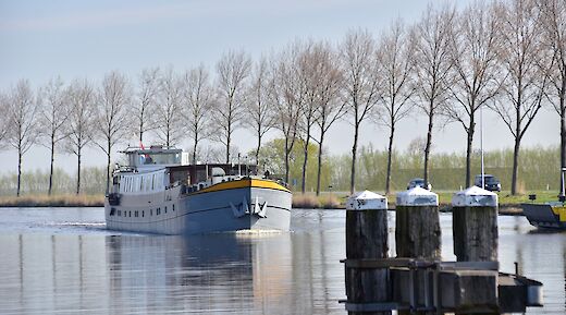 A boat named Lena Maria approaches on a canal with a line of trees in the distance.