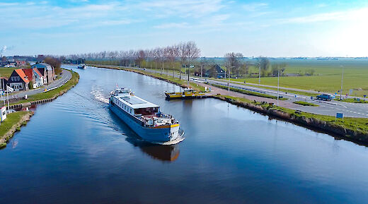 A boat named Lena Maria sails on a canal with houses and farmland in the background.