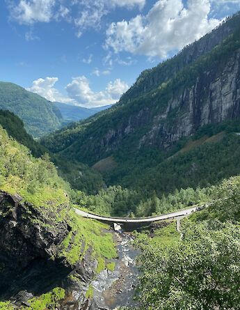 A bridge spanning a valley with a river below, surrounded by lush green mountains in Voss, Norway.