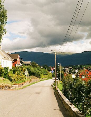 A road in Voss, Norway, lined with colorful houses and trees, under a cloudy sky.