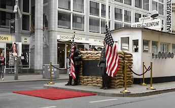 American flags displayed at Checkpoint Charlie in Berlin, Germany, near a historical guardhouse replica.