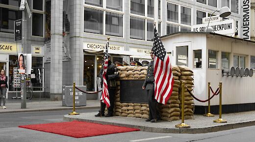 American flags displayed at Checkpoint Charlie in Berlin, Germany, near a historical guardhouse replica.