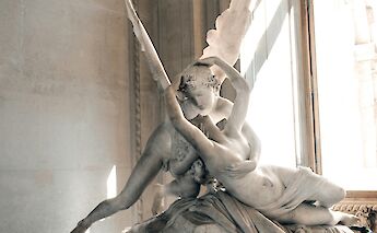 Statue of Cupid and Psyche indoors, with soft lighting illuminating the detailed figures.