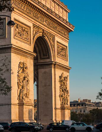 Arc de Triomphe at dusk, Paris, France, capturing the monument bathed in warm sunlight with cars passing below.