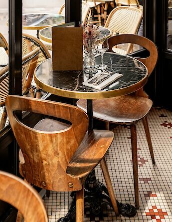A set table at a Parisian café with wooden chairs, a marble tabletop, and glassware, situated indoors by a window.