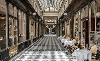 Grand cafe with outdoor seating in a historic Parisian arcade.