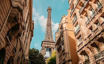 Looking up at the Eiffel Tower from a Paris street, framed by historic buildings.