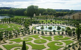 The intricate geometric gardens of the Palace of Versailles, featuring manicured lawns and fountains.