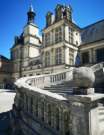 Stone steps leading to Fontainebleau Castle, France. The historic building features a clock tower and ornate architecture under a clear blue sky.