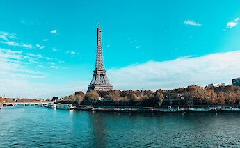View of the Eiffel Tower on a sunny day, seen from across the Seine River in Paris, France.
