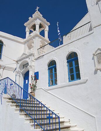 A white-washed building with blue accents and a belfry, featuring a staircase with blue railings.