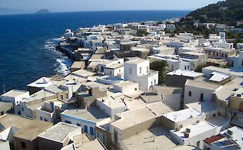 A coastal view of the town of Mandraki on the island of Nisyros, Greece, featuring traditional white buildings and the nearby sea.