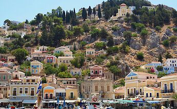 Colorful hillside houses among greenery on the Island of Symi, Greece.
