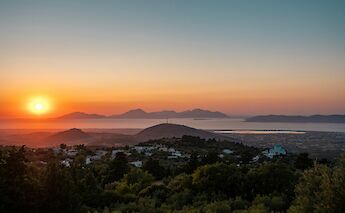 Sunset view over Kos Island, Greece, with rolling hills and the sea in the distance.