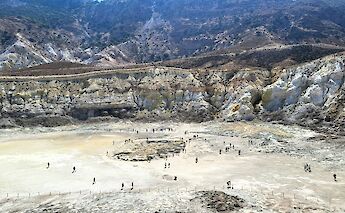 A volcanic crater with visitors walking on its surface, located on the island of Nisyros, Greece.