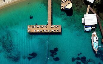 An aerial view of turquoise water with a wooden dock and boats, located in Bodrum, Turkey.