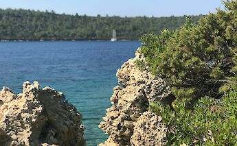 View of green foliage and rocky formations framing a distant coastline and water in Bodrum, Turkey.