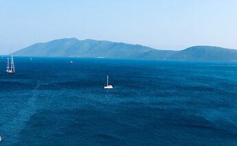 A sailboat in the distance on a deep blue sea with mountainous coastline on the horizon, viewed from Bodrum, Turkey.