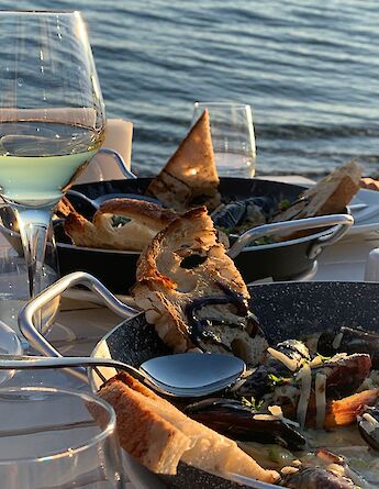 Outdoor dining by the waterfront in Bodrum, Turkey, featuring meals with bread and a glass of white wine.