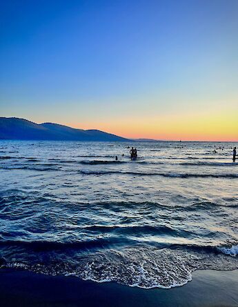 People swimming in the sea at sunset with silhouettes against the horizon in Akyaka, Turkey. Mountains are visible in the background.