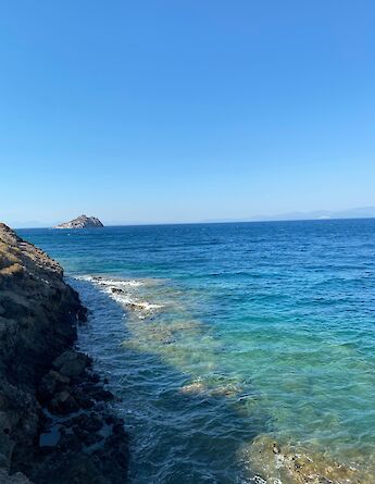 Rocky coastline with clear blue water and a small island in the distance, viewed from Bodrum, Turkey.
