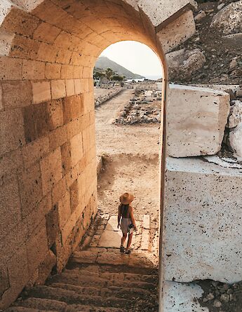 A woman walking down ancient stone steps through an archway, leading to ruins in Knidos, Turkey.