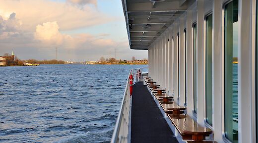 The side view of the boat "Lisabelle," showing a walkway alongside windows, with a river and distant shoreline.