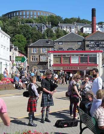 1. Bagpipers perform on a street in Oban, Scotland, with McCaig's Tower visible in the background.