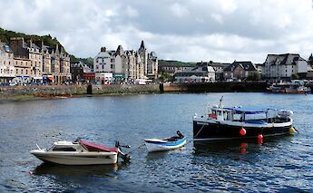 Boats docked in the water near the harbor of Oban, Scotland, with historic buildings along the waterfront.