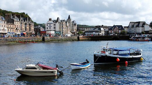 Boats docked in the water near the harbor of Oban, Scotland, with historic buildings along the waterfront.