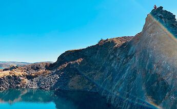 A rocky cliff with a person standing on top, set against a clear blue sky in Oban, Scotland.