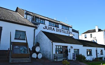 4. Jura Distillery's white buildings with barrels outside, under a clear blue sky in Scotland.