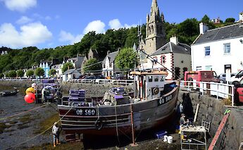 Colorful houses and a church line the waterfront in Tobermory, Isle of Mull, Scotland, with a fishing boat in the foreground.