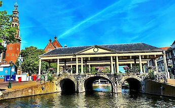 A covered stone bridge over a canal, with bicycles parked along the railing, and historic buildings in the background.