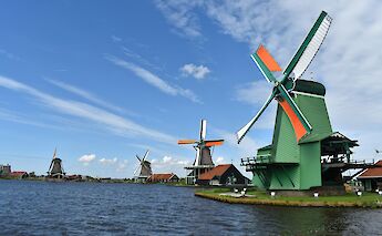 Windmills along a waterfront against a blue sky at Zaanse Schans, Holland.
