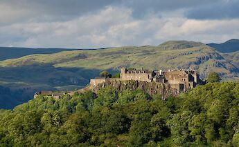 Stirling Castle in Scotland, set against rolling green hills and surrounded by dense forests.