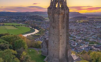 The Wallace Monument on a hill overlooking Stirling, Scotland, with a river winding through the landscape at sunset.