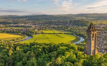 - Aerial view of the Wallace Monument in Stirling, Scotland, surrounded by green fields and a winding river.