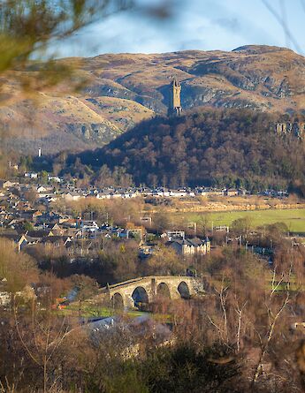 A town nestled in a valley with a hillside covered in trees; the Wallace Monument is visible amidst the landscape.