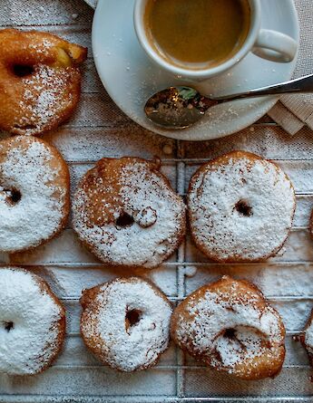 A cup of coffee and dutch fried dough balls dusted with powdered sugar. BernFresen@unsplash
